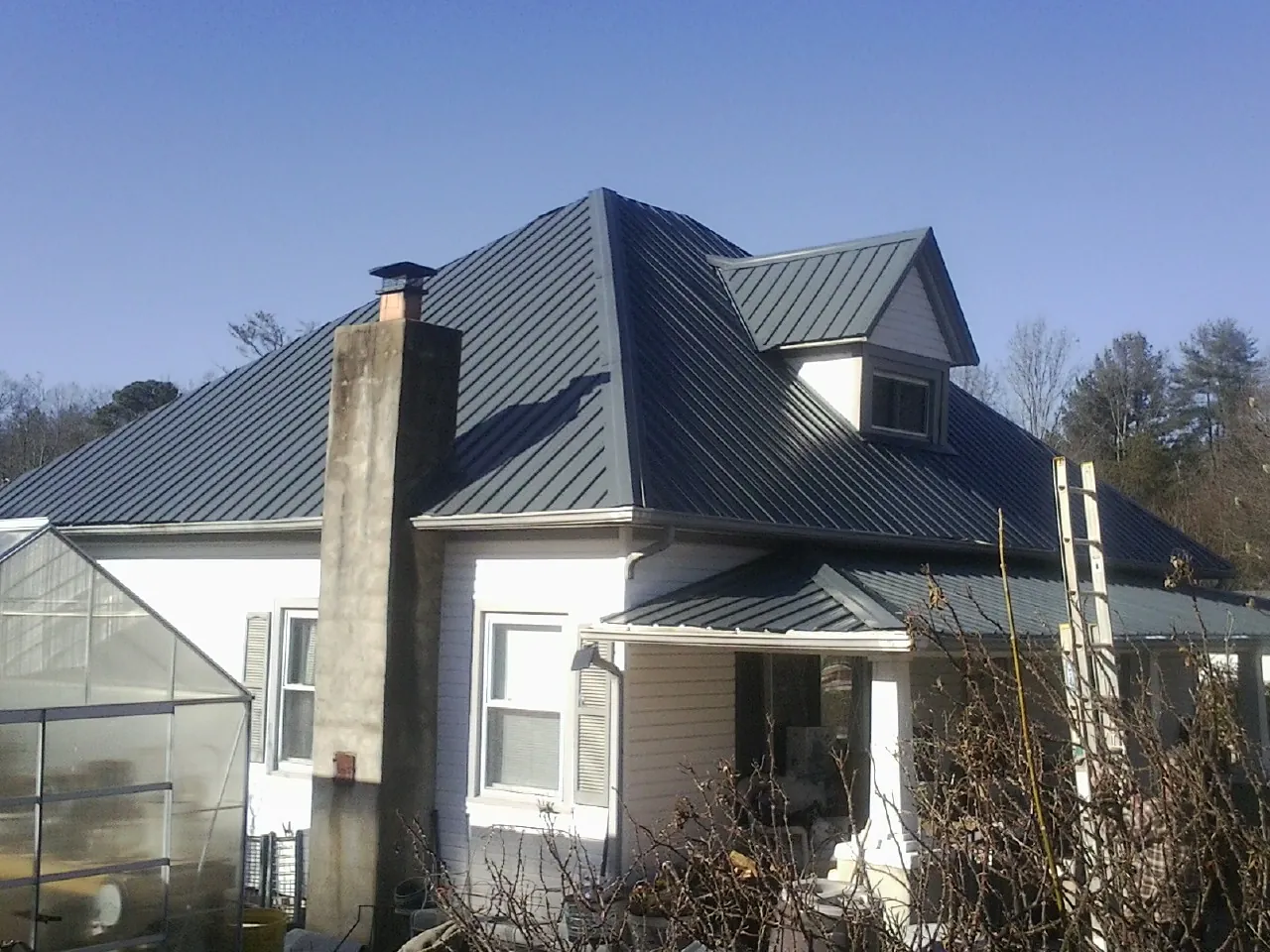 Dark blue standing seam metal roof on a white farmhouse with dormer — Slate & Tile Roof Repair by Roofing Brothers in Mcleod