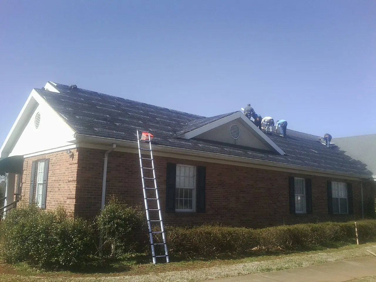 Crew tearing shingles off a brick ranch roof with a ladder set — Metal Roof Repair work by our crew in Mcleod