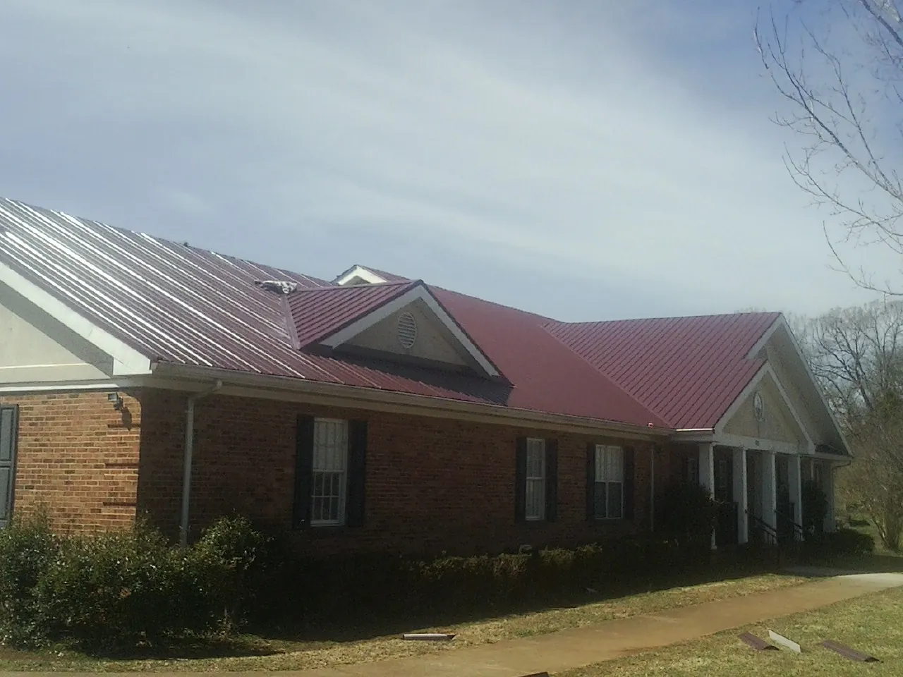 Red metal roof with gabled entries on a long brick building, from a Hail Damage Roof Repair job in Mcleod