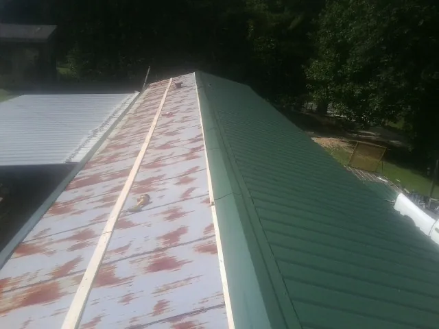 Old rusted panels beside newly installed green metal roofing — Wind Damage Roof Repair by Roofing Brothers in Mcleod