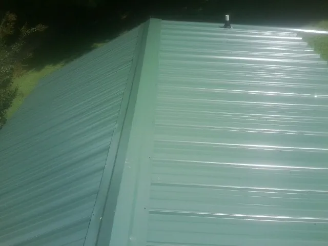 New green metal panels meeting at the ridge of a roof — Flat Roof Repair work by our crew in Mcleod